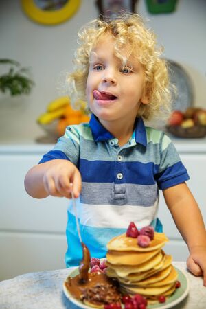 Little curly boy eating sweet pancakesの写真素材