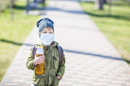 A boy in mask holds a bottle of water in handの写真素材
