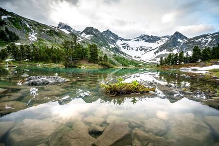 Green lake between mountains in cloudy dayの写真素材