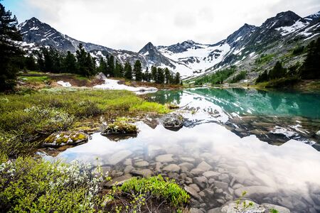 Green lake between mountains in cloudy dayの写真素材
