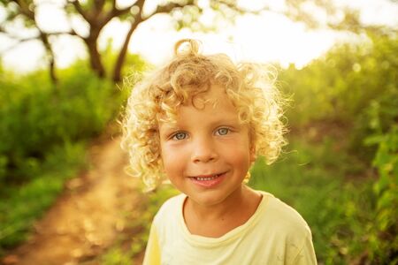 Portrait of a curly white boy in the park in sunset timeの写真素材