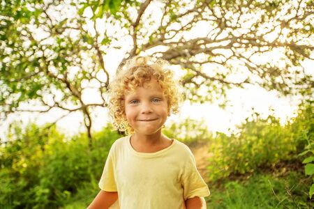 Portrait of a curly white boy in the park in sunset timeの写真素材