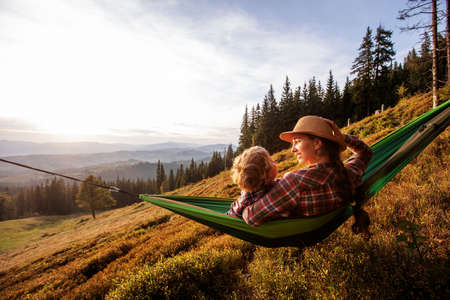 Boy with mom resting in a hammock in the mountains at sunsetの写真素材