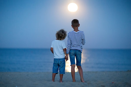 two boys look at the moon by the seaの写真素材