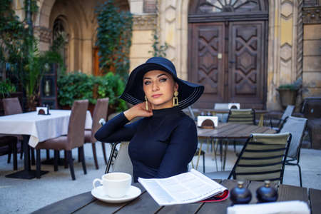 Exquisite woman in a black hat drinks coffeeの写真素材