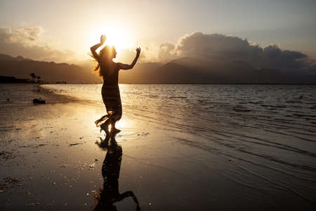 Beautiful woman dancing by the sea at sunsetの写真素材