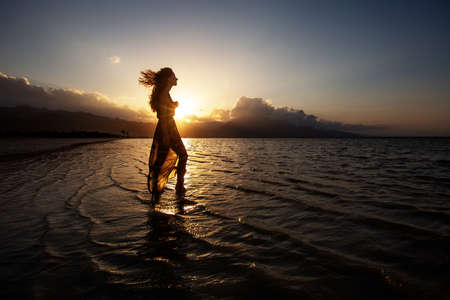 Beautiful woman dancing by the sea at sunsetの写真素材
