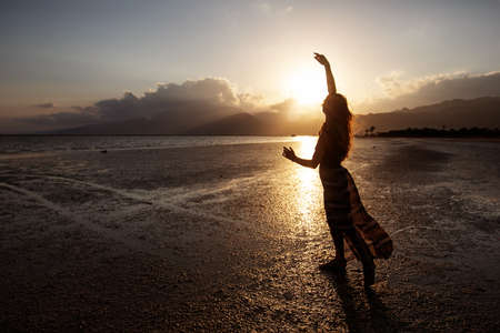 Beautiful woman dancing by the sea at sunsetの写真素材