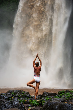 Beautiful woman doing yoga near a waterfall in Baliの写真素材