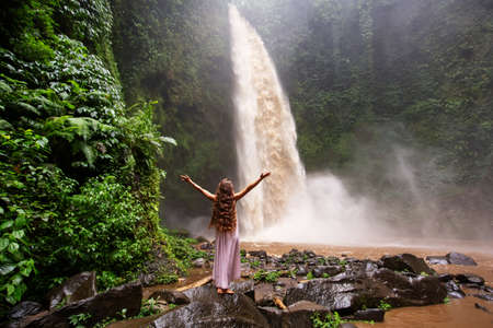 Beautiful woman in a pink dress near a waterfall in Baliの写真素材