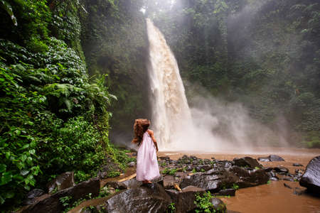 Beautiful woman in a pink dress near a waterfall in Baliの写真素材