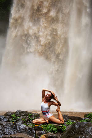 Beautiful woman doing yoga near a waterfall in Baliの写真素材