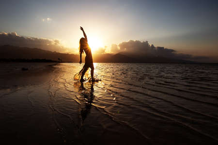 Beautiful woman dancing by the sea at sunsetの写真素材