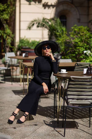 Exquisite woman in a black hat drinks coffeeの写真素材