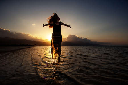 Beautiful woman dancing by the sea at sunsetの写真素材