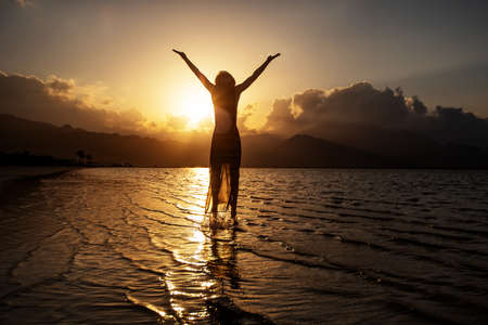 Beautiful woman dancing by the sea at sunsetの写真素材
