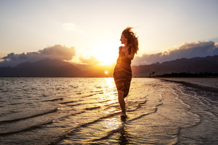 Beautiful woman dancing by the sea at sunsetの写真素材