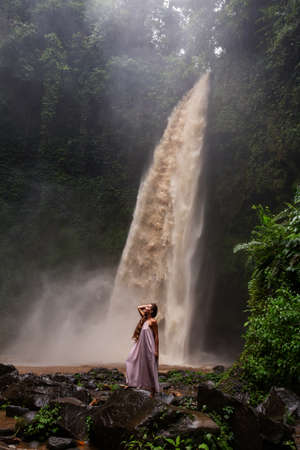 Beautiful woman in a pink dress near a waterfall in Baliの写真素材