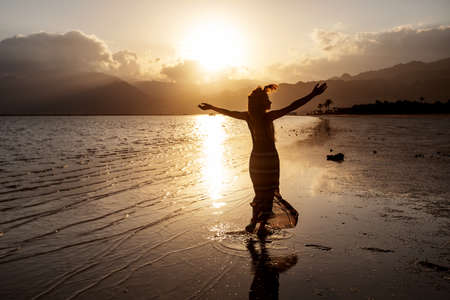 Beautiful woman dancing by the sea at sunsetの写真素材