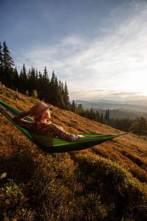 Woman hiker resting after climbing in a hammock at sunsetの写真素材