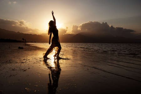Beautiful woman dancing by the sea at sunsetの写真素材