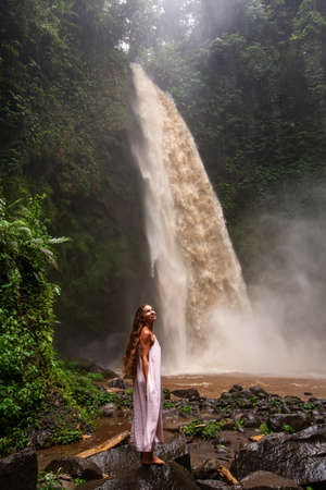 Beautiful woman in a pink dress near a waterfall in Baliの写真素材
