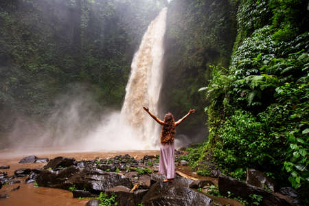 Beautiful woman in a pink dress near a waterfall in Baliの写真素材