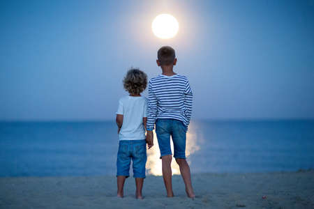 two boys look at the moon by the seaの写真素材