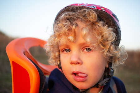 White curly boy in a helmet in a bicycle seatの写真素材