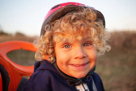 White curly boy in a helmet in a bicycle seatの写真素材