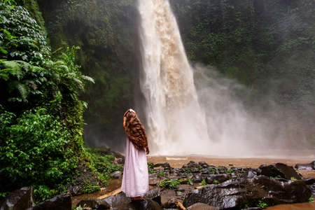 Beautiful woman in a pink dress near a waterfall in Baliの写真素材