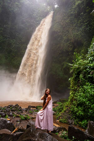 Beautiful woman in a pink dress near a waterfall in Baliの写真素材