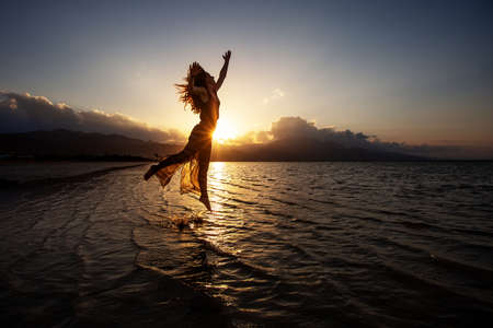 Beautiful woman dancing by the sea at sunsetの写真素材