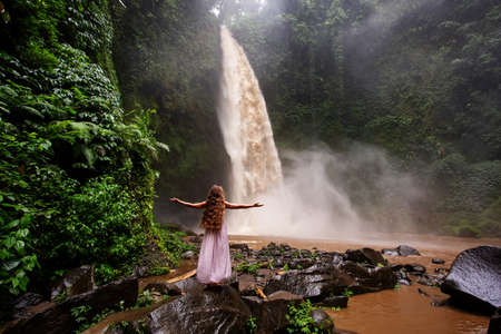 Beautiful woman in a pink dress near a waterfall in Baliの写真素材