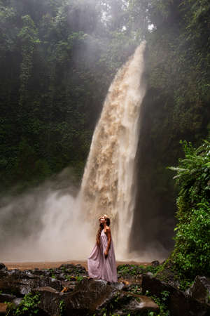 Beautiful woman in a pink dress near a waterfall in Baliの写真素材