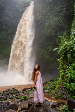 Beautiful woman in a pink dress near a waterfall in Baliの写真素材