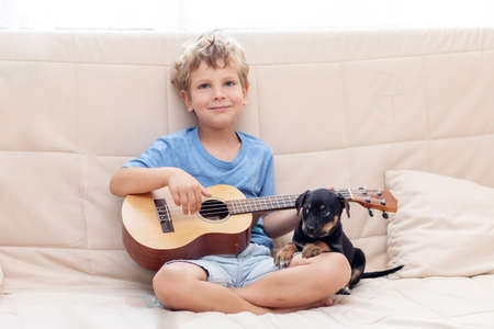 A boy with a small dog playing the ukuleleの写真素材