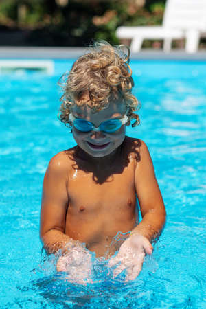 Curly boy in the pool with glassesの写真素材