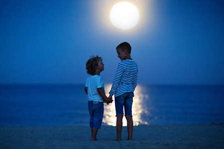 two boys look at the moon by the seaの写真素材