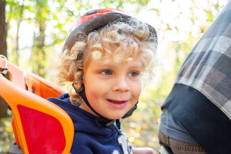White curly boy in a helmet in a bicycle seatの写真素材