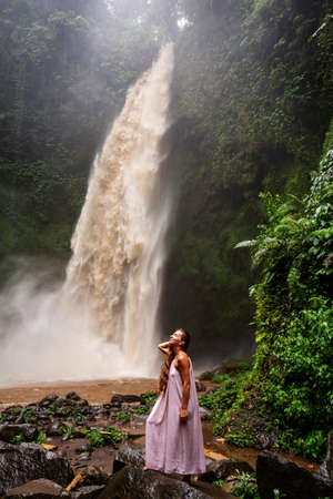Beautiful woman in a pink dress near a waterfall in Baliの写真素材