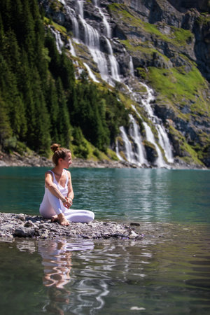 A woman practices yoga in the mountains in Switzerland on Lake Oeschinenseeの写真素材