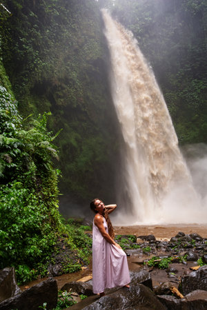 Beautiful woman in a pink dress near a waterfall in Baliの写真素材