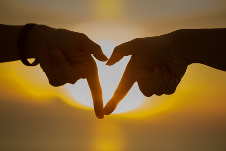 Silhouette hand in heart shape during sunsetの写真素材