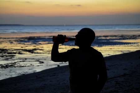 Man drinking a cold beer on a beach at sunsetの写真素材