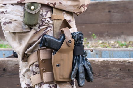 camouflaged soldier in military uniform with gun holstered to his waist