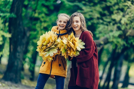 Two sisters hug, with a bunch of leaves in the park.