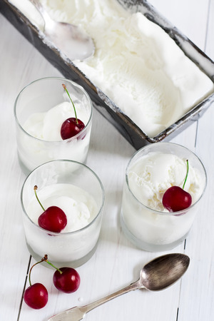 Homemade vanila ice cream in frozen metalic container and glasses with ripe red cherry. Selective focus.の写真素材