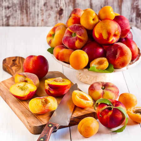 Ripe apricots, nectarines and saturn peaches on ceramic holder and olive wood desk with knife. の写真素材