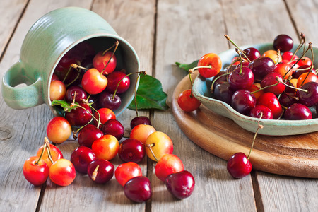 Ripe sweet mixed cherry in lying teal cup and on a saucer on old wooden table. Selective focus.の写真素材